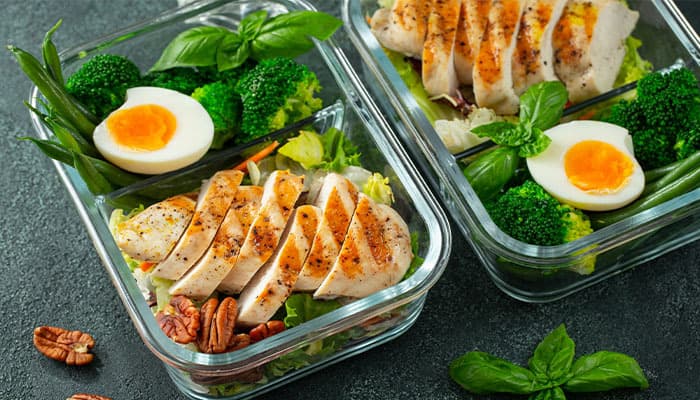 two meal prep bowls with chicken and greens